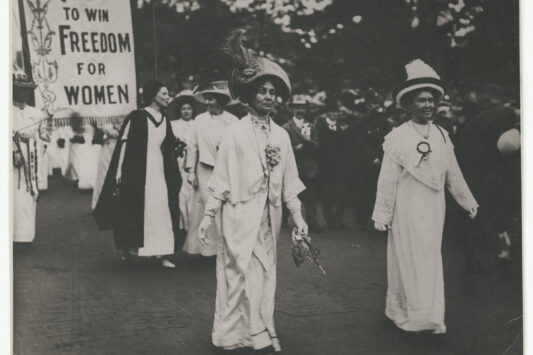 British Suffragettes walking down the street carrying signs.