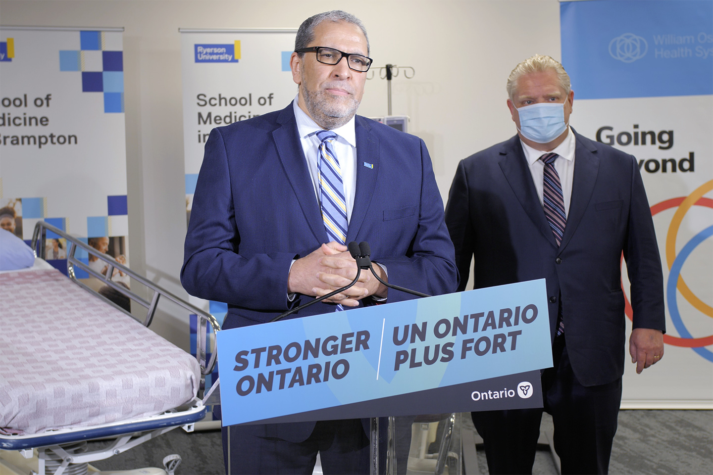 TMU President Mohamed Lachemi stands at a podium displaying a sign that reads Stronger Ontario with the Province of Ontario logo. Toronto Premier Doug Ford stands behind him wearing a mask.