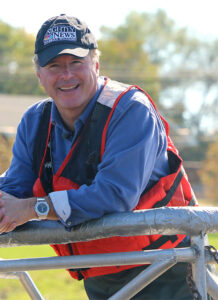 Kevin Tibbles, Journalism ’79, posing in blue shirt and orange vest.