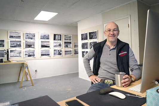 Vince Lupo sitting at his workspace with his photography in the background.
