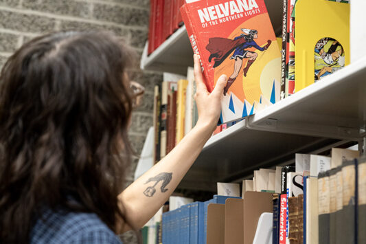 A woman pulls a comic from a library shelf.
