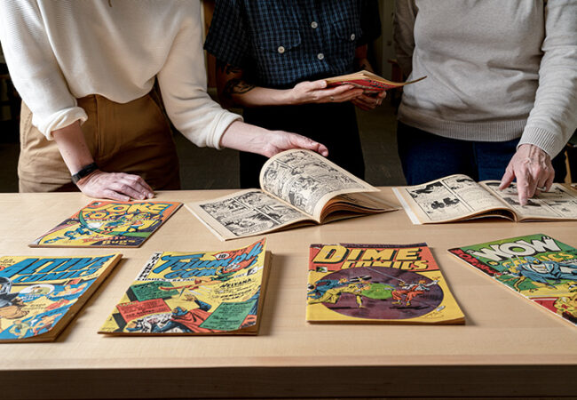 Three people look through comics laid out on a table in front of them.