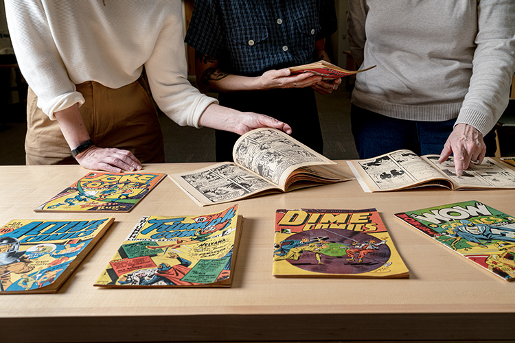 Three people look through comics laid out on a table in front of them.