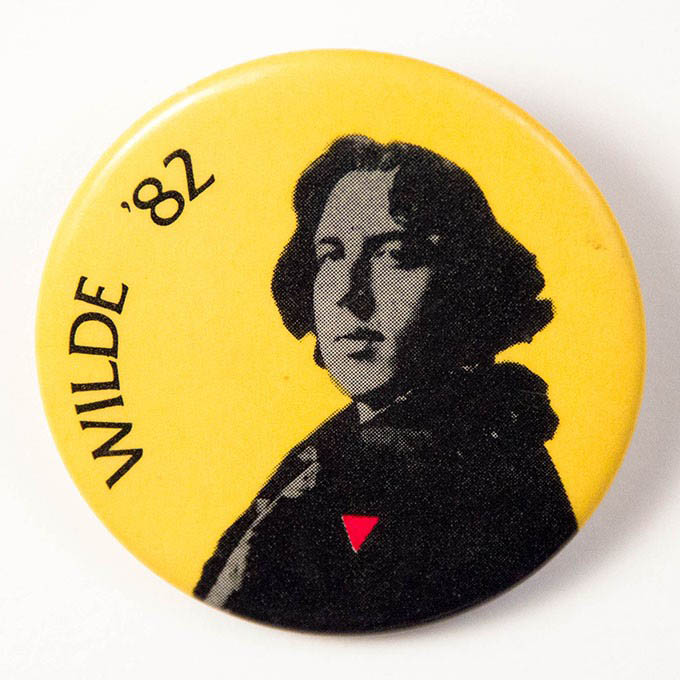 Circular yellow button with a black and white image of Oscar Wilde wearing an upside down pink triangle instead of his usual carnation.