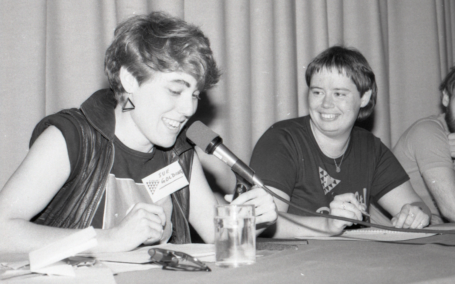 Two young women seated at a table talk into a microphone.