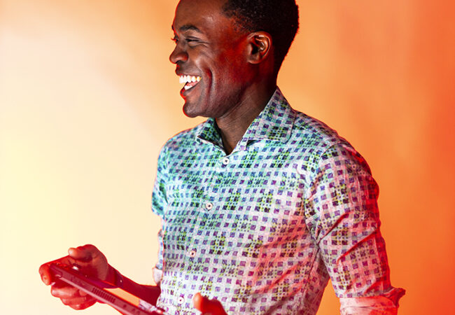 Kristopher Alexander smiling in a brightly coloured, checkered shirt.