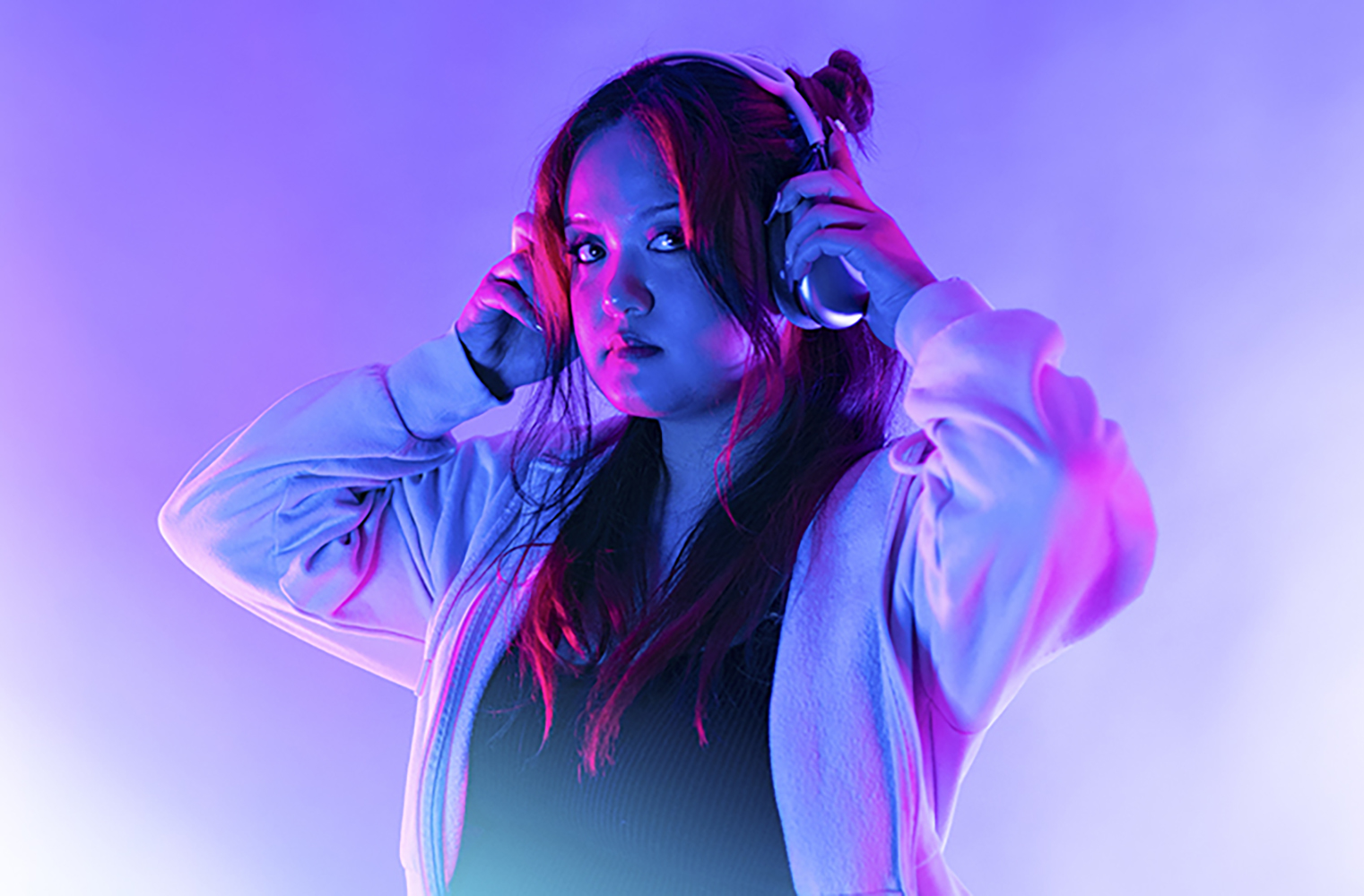 Sofia Beltran stands in a hooded sweatshirt with headphones on, looking at the camera.
