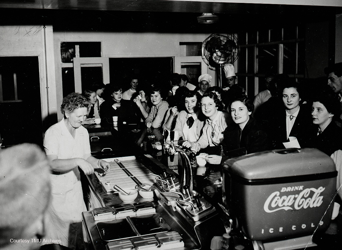 Crowd of students around the bar with a woman scooping ice cream.