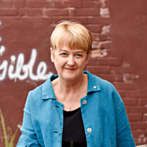 Cathy Crowe in a blue shirt in front of a brick wall.