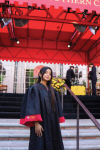 Eemaan Qadri wearing a USC robe stands on stairs under an awning.