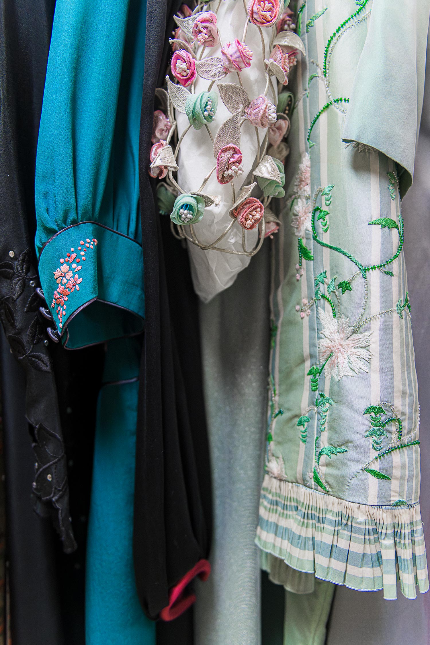 The sleeves of a row of dresses hanging up together. One is blue, one is cream with flowers, one is light blue and green.