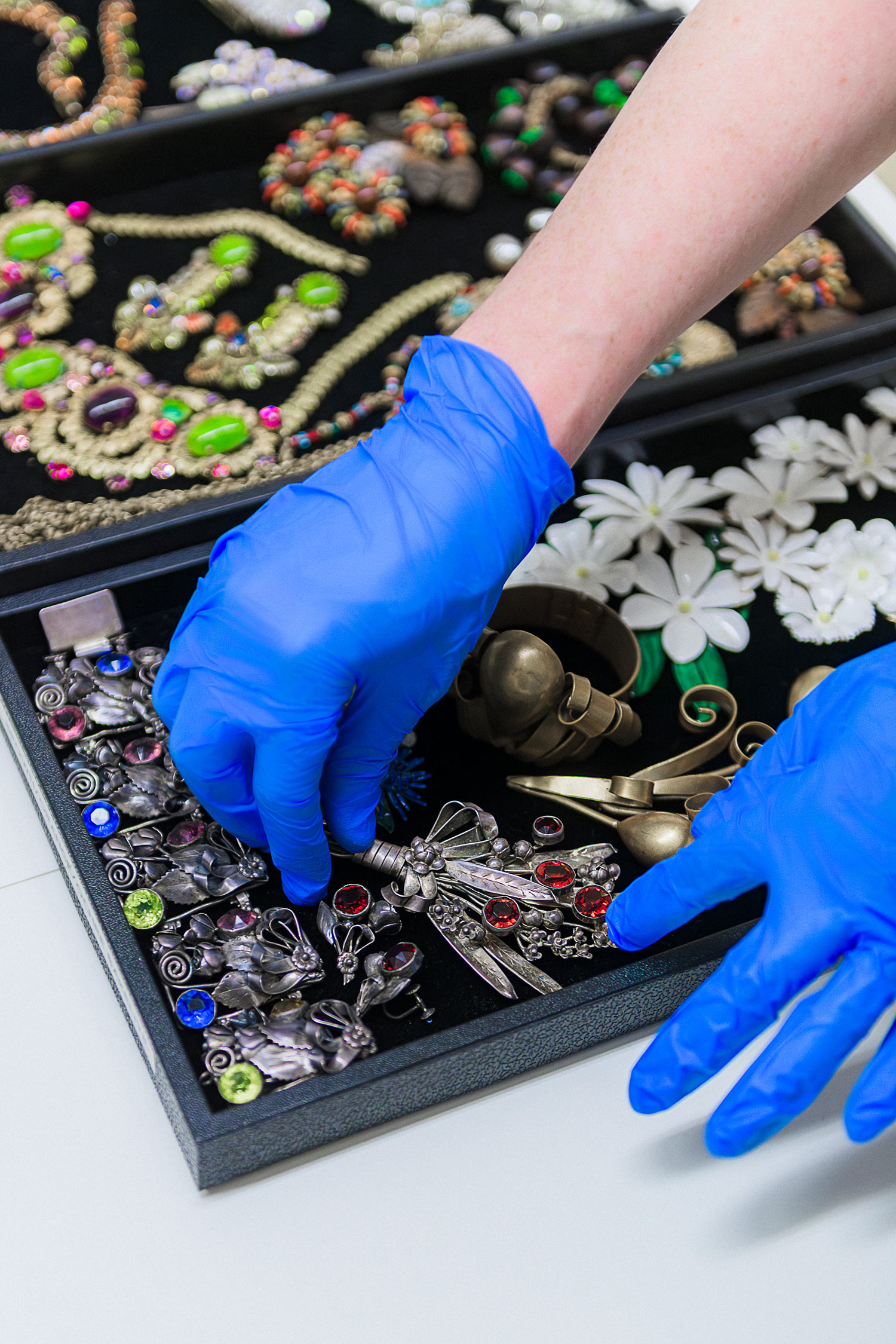 Hands wearing blue protective gloves arrange a collection of jewelry in a black box.