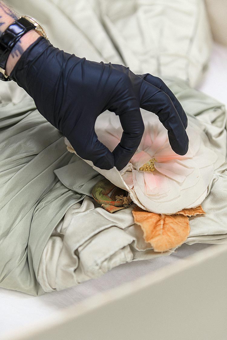 A hand in a black glove gently touches a flower appliqué on a garment.