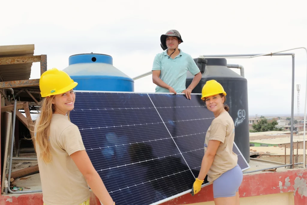 Three people hold a solar panel, ready for installation.