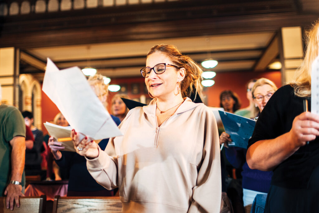 A woman stands at the front of a choir and sings.