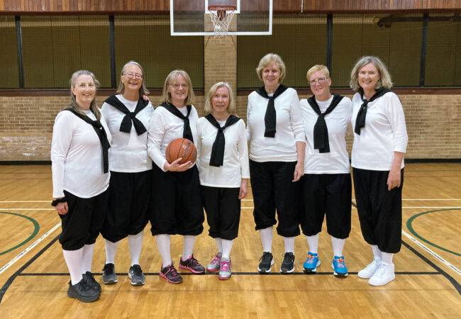 A group of senior women standing on a basketball court together.