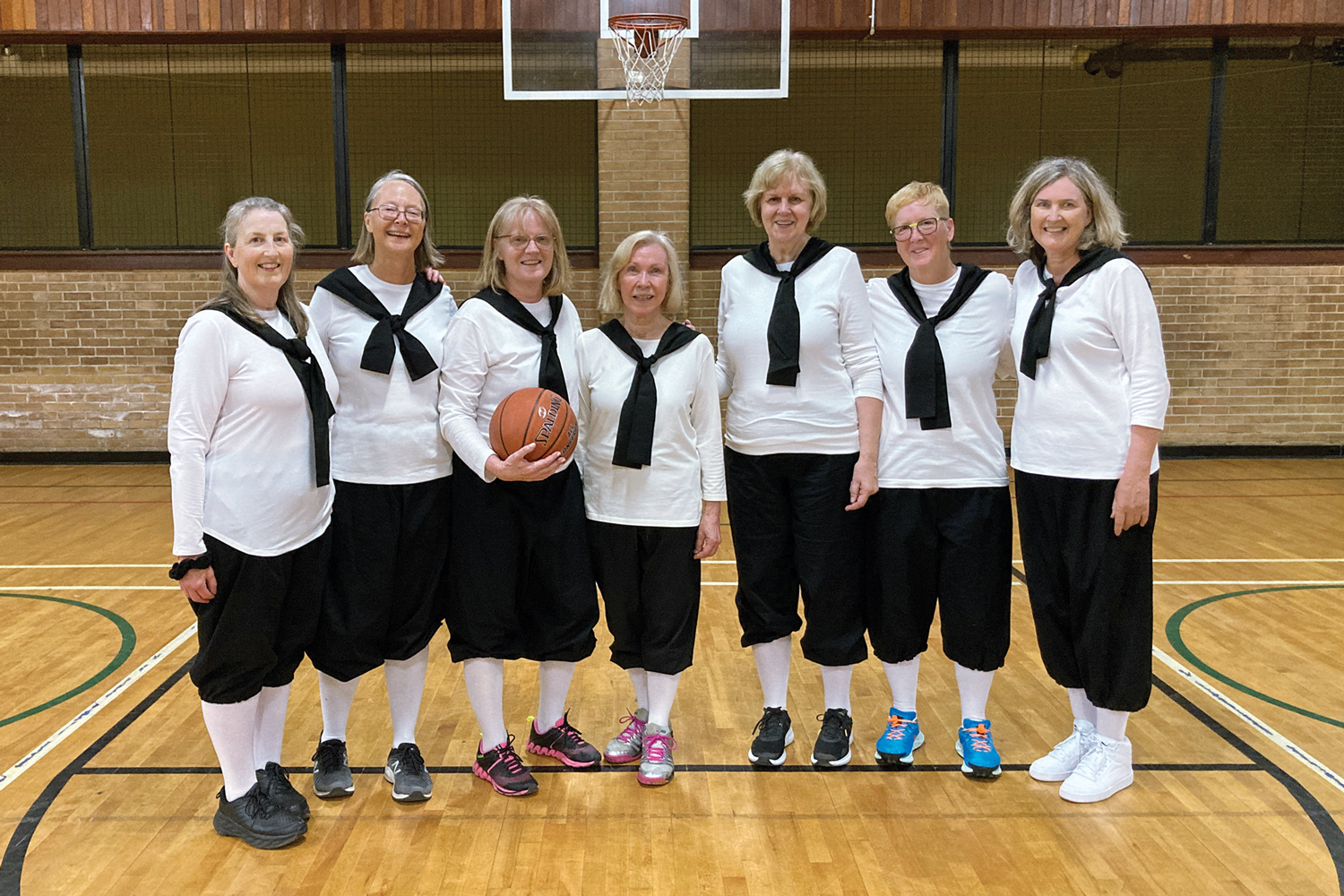 A group of senior women standing on a basketball court together.