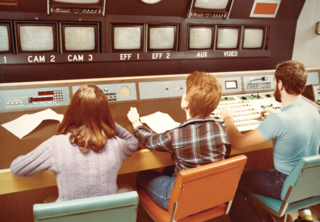 Three university students sit in a 1970s television control room.