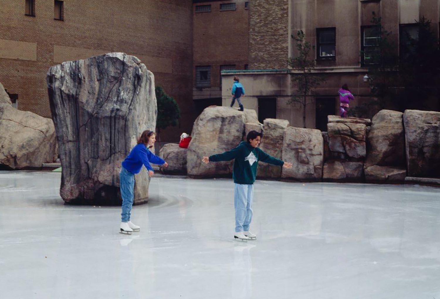 Two girls skating on the frozen Lake Devo surface with arms spread wide.