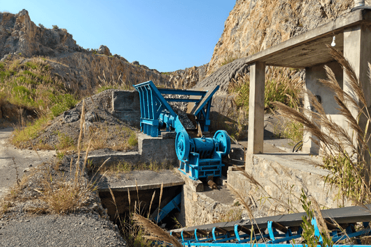 A blue machine used for crushing blasted rock sits in an abandoned mine and mountain range in Pakistan.