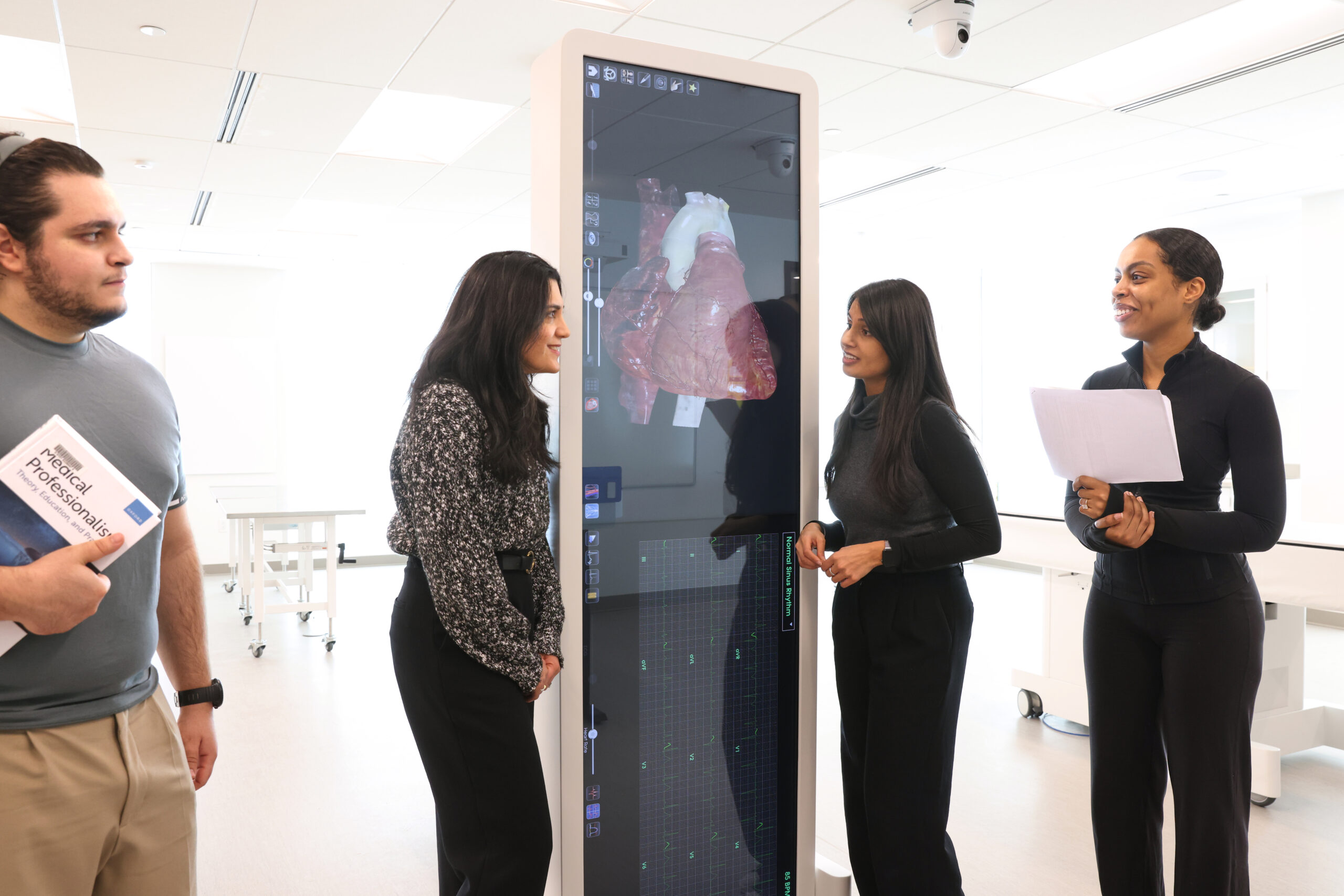 Medical students and faculty clinician chat with the anatomy lab director while she shows them a digital anatomical model.