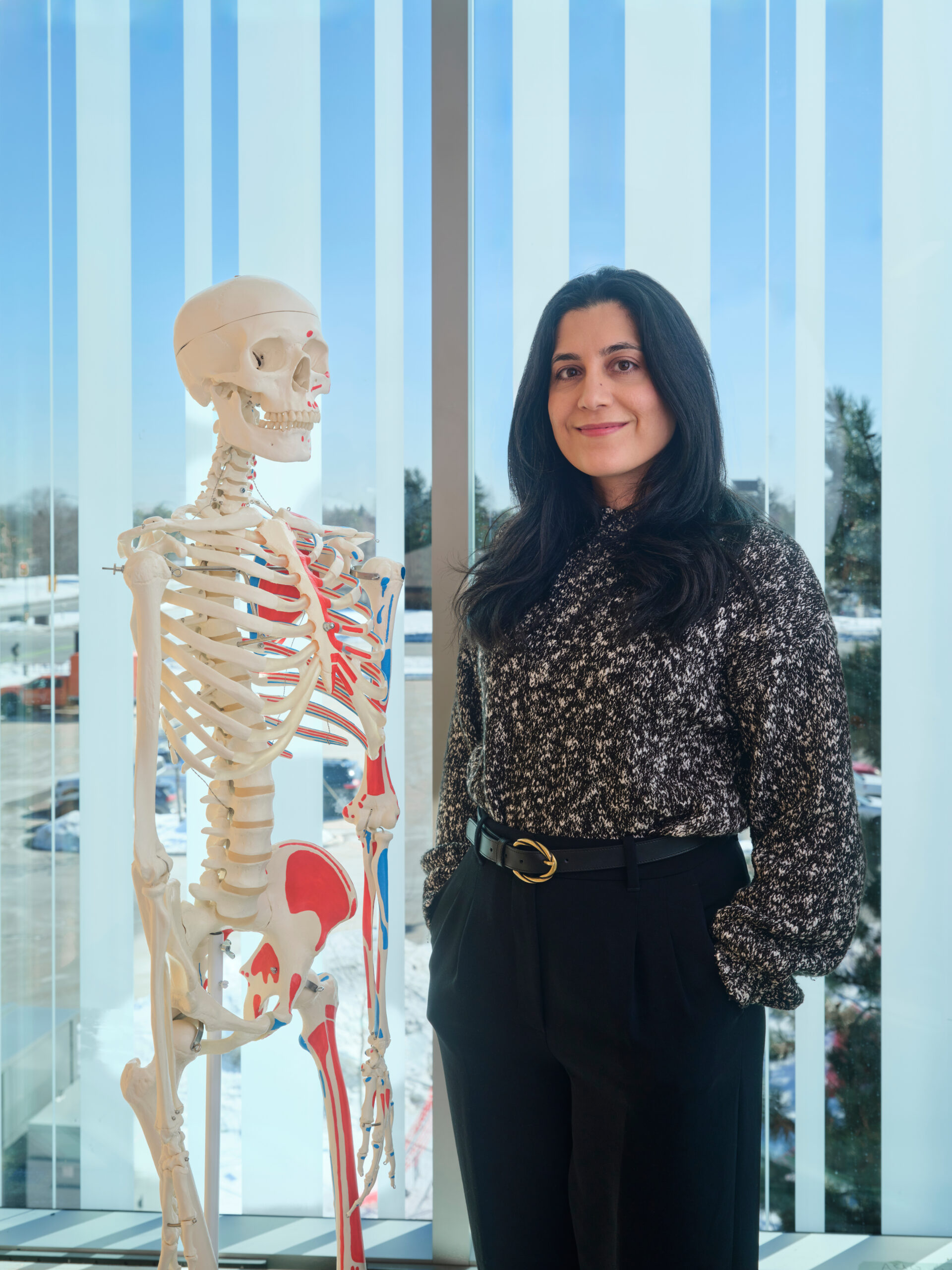 Dr. Mehry Kianfar stands next to a medical school skeletal model.