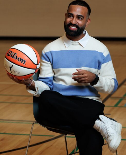 Kishan Mistry smiling while seated with a basketball in his hand.