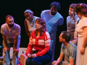 A group of people on stage looking toward an actor in the middle.