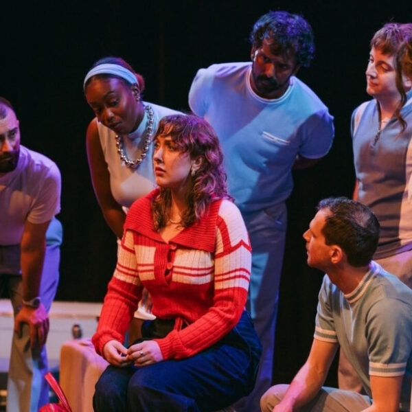A group of people on stage looking toward an actor in the middle.