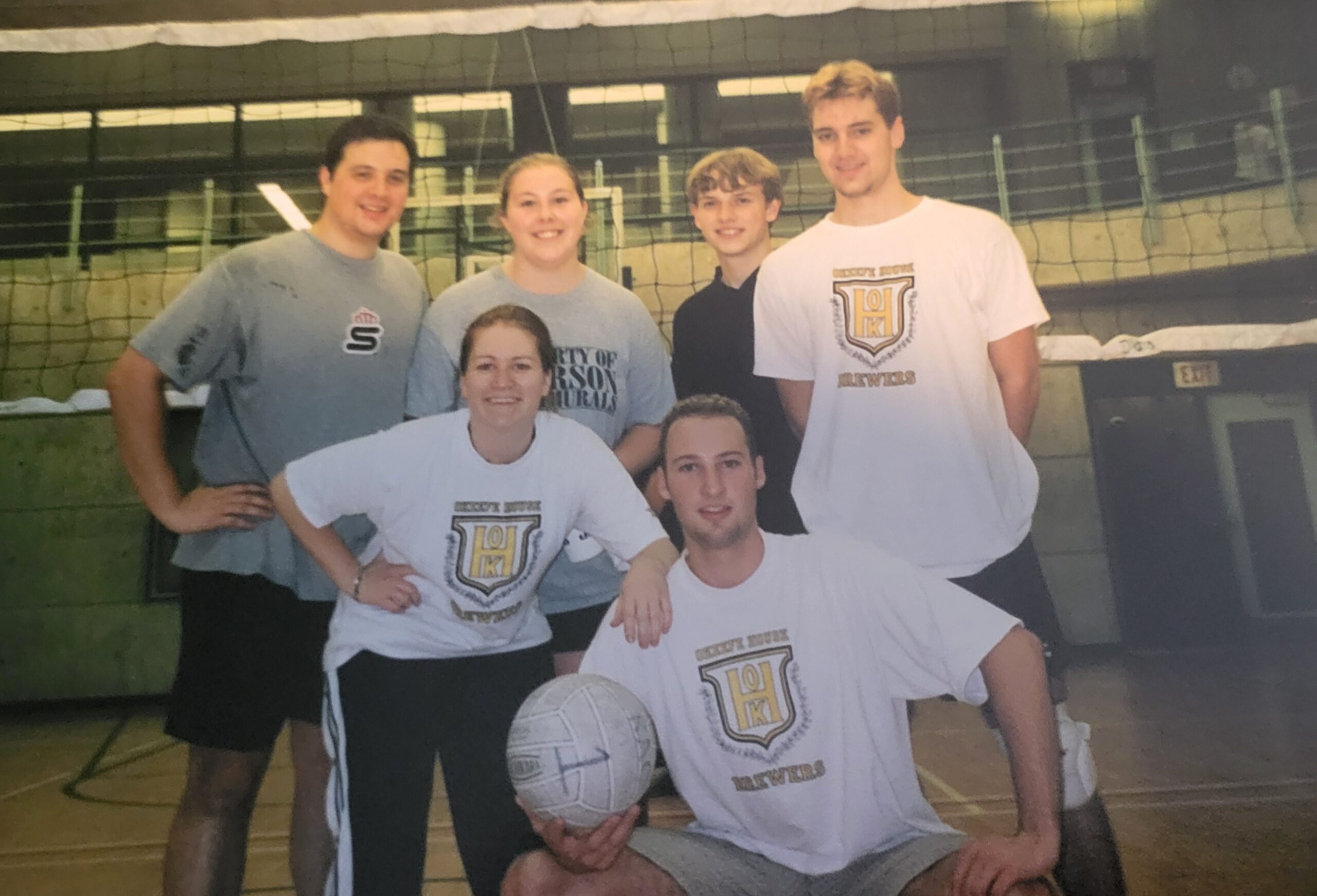 Six people pose for a photo after playing a volleyball game.