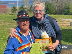 Two people pose outside on a sunny day with a book in hand.