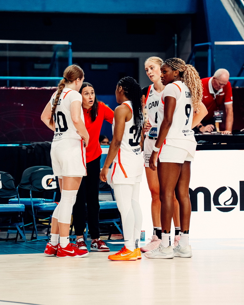 Carly Clarke speaks to players in Team Canada jerseys from the sideline.