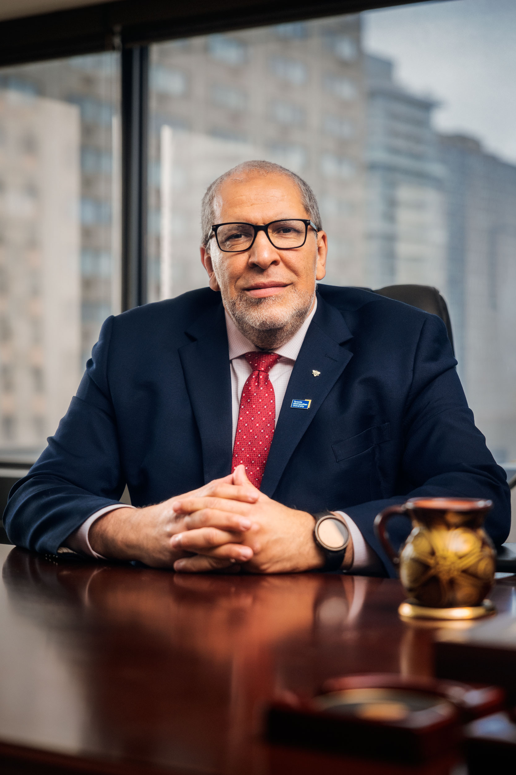 Mohamed Lachemi seated at a table in a navy suit and red tie, with a Toronto Metropolitan University pin on his lapel.