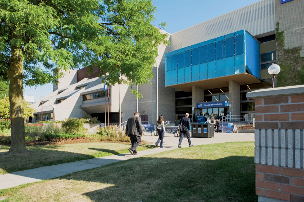 People walk toward the entrance of a TMU School of Medicine building with a bright blue exterior feature.