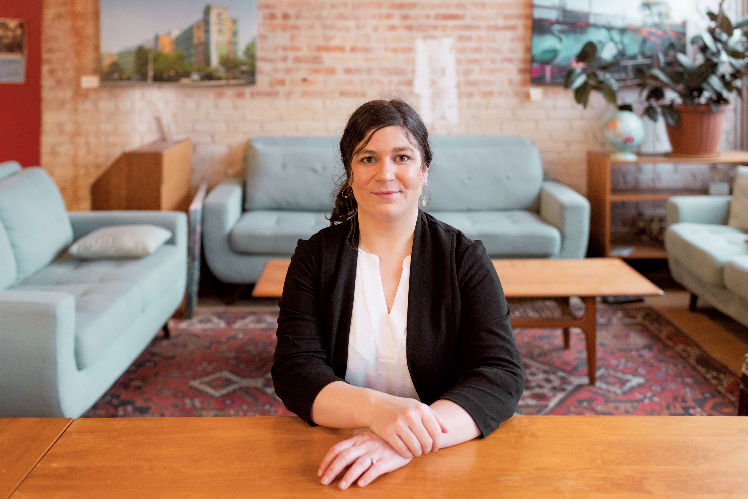 Desneige Frandsen seated at a wooden table in front of a couch, wearing a black cardigan and white blouse.